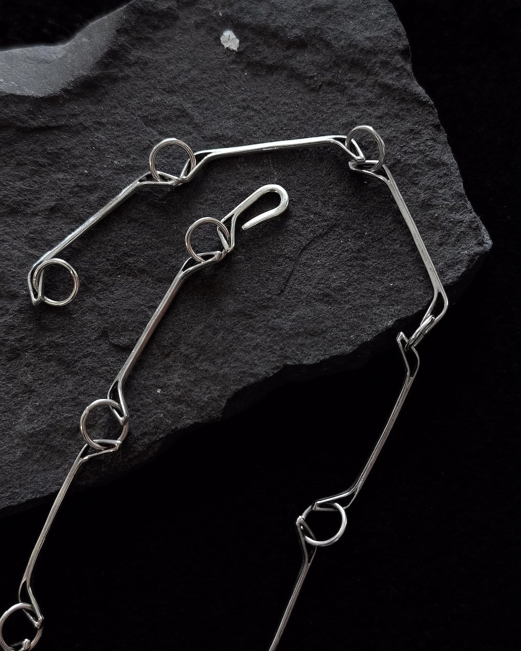 Minimalist sterling silver necklace lying on a stone, sculptural design inspired by a horse jawbone